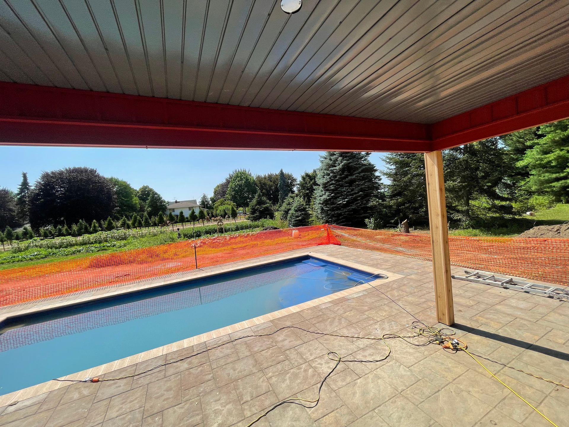 Covered patio with a rectangular pool, surrounded by orange safety fencing and a grassy yard.