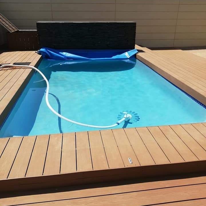 A rectangular pool with a blue cover and a robotic cleaner surrounded by a wooden deck.