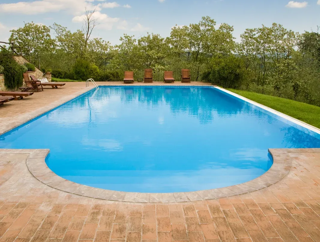 A view of a rectangular pool with blue water and surrounding red construction fencing; trees and sky in the background.