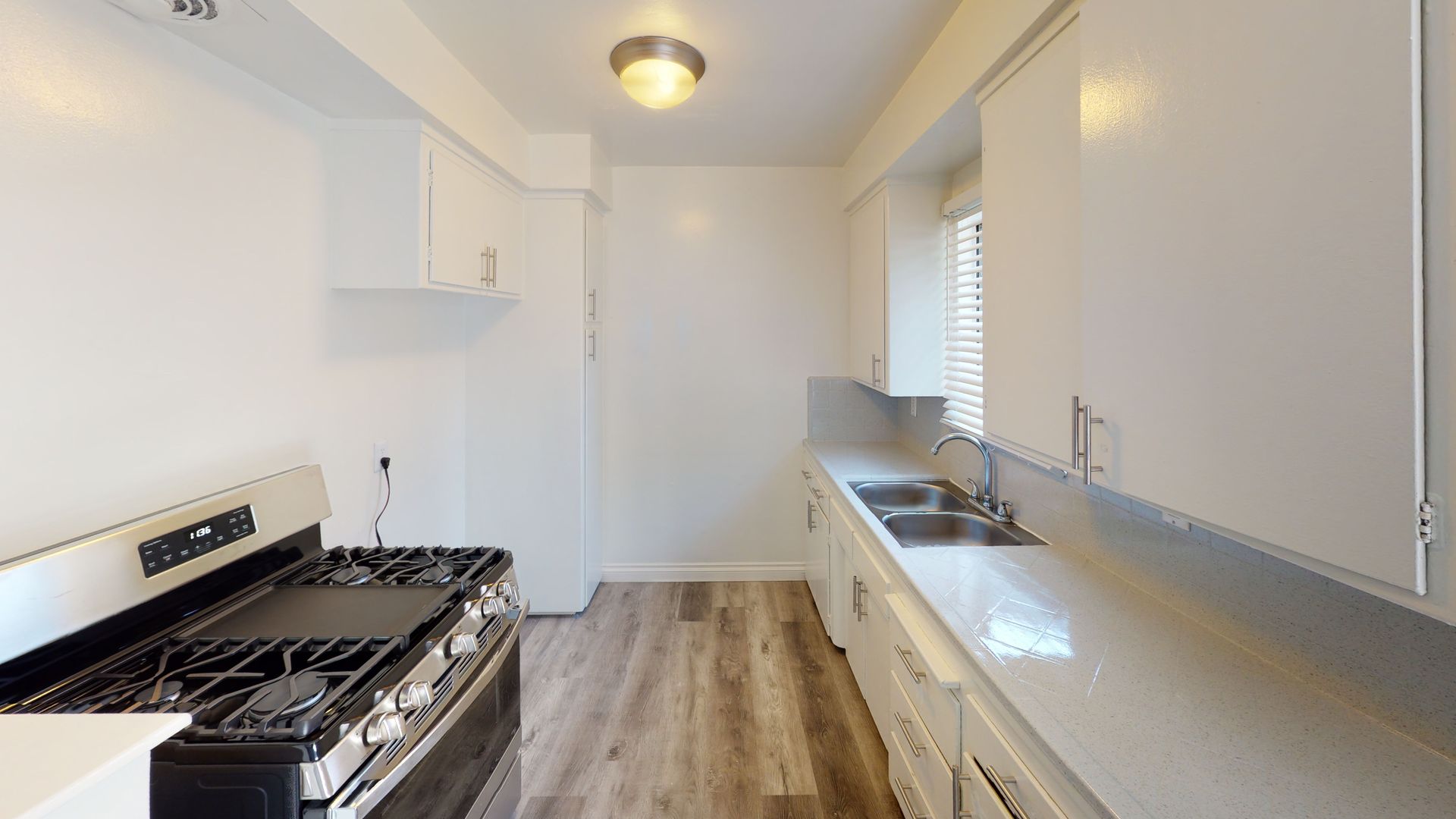 Kitchen with white cabinets, stove, sink, and wood-look flooring.