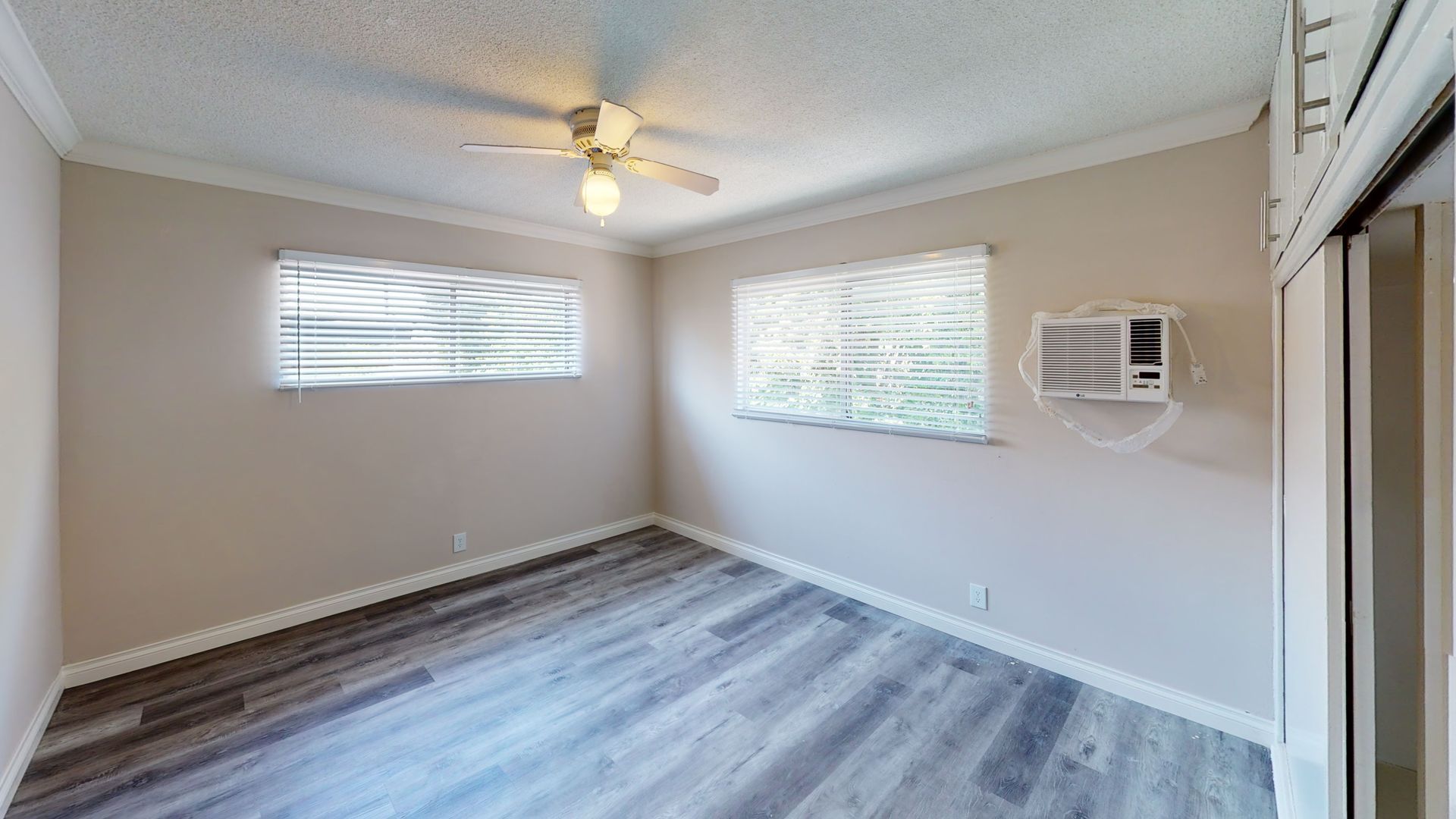 Empty bedroom with grey flooring, two windows, and an AC unit.