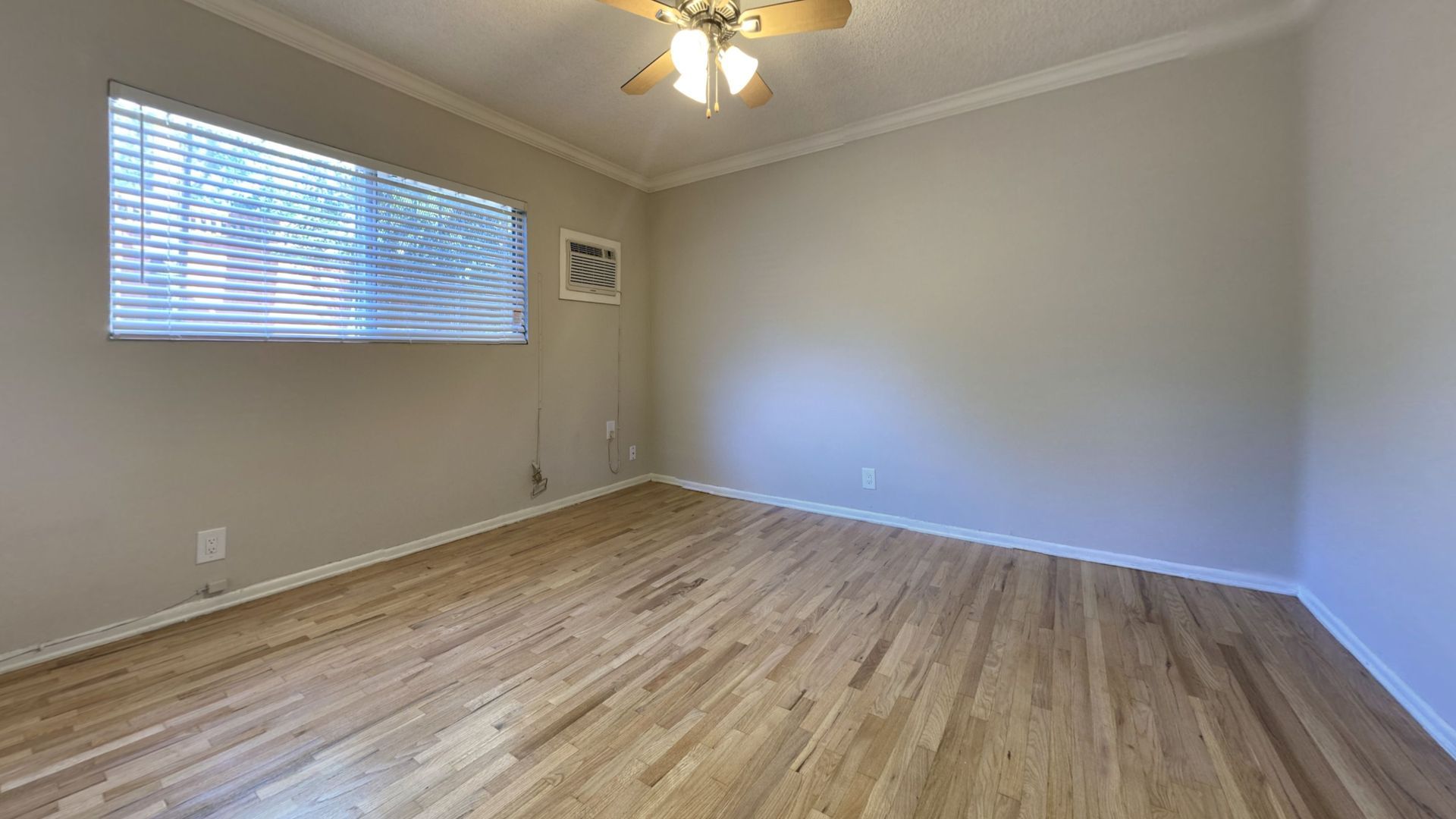 Empty room with hardwood floors, a window with blinds, and a ceiling fan.