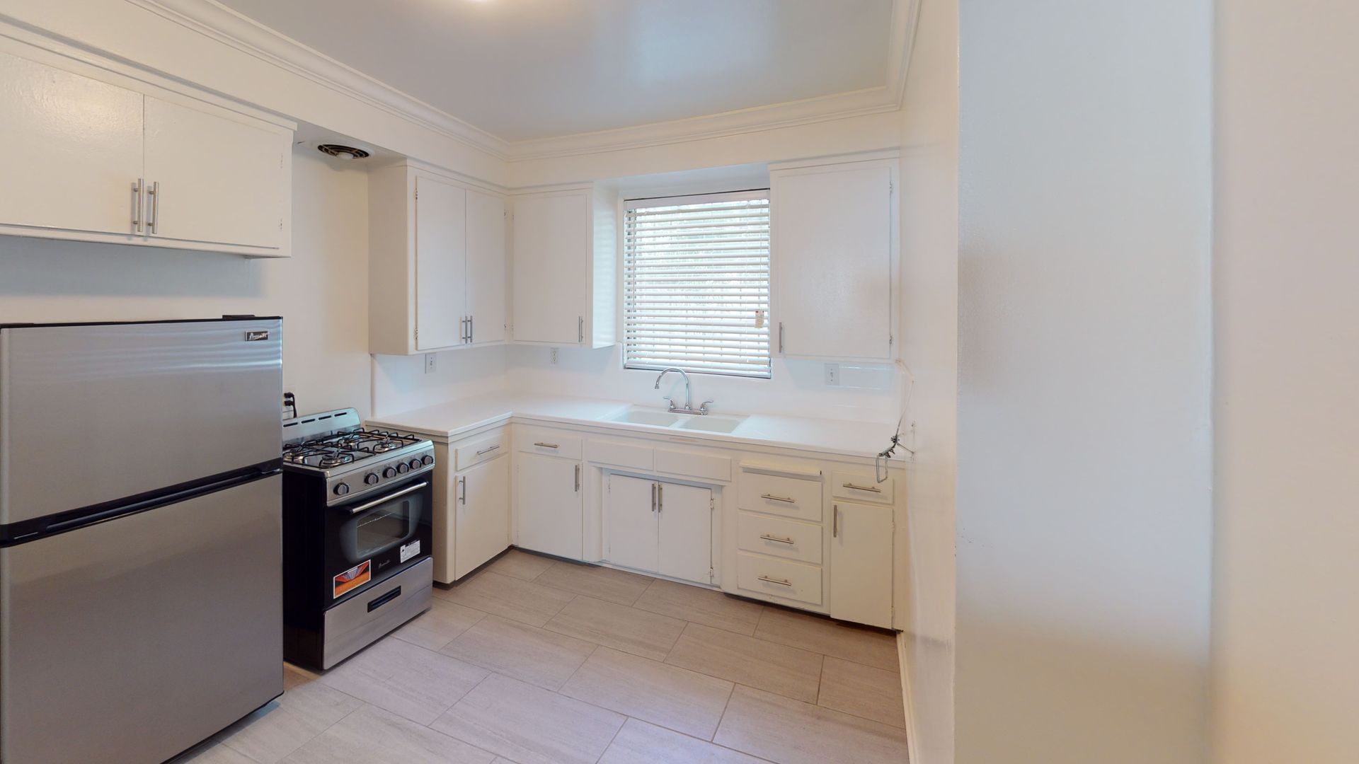 White kitchen with stainless steel appliances, white cabinets, and a window.