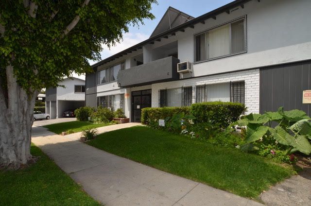 Apartment building with a gray and white exterior, green lawn, and sidewalk.