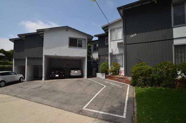 Apartment building exterior, with parking and multiple floors. Gray and white buildings under a blue sky.