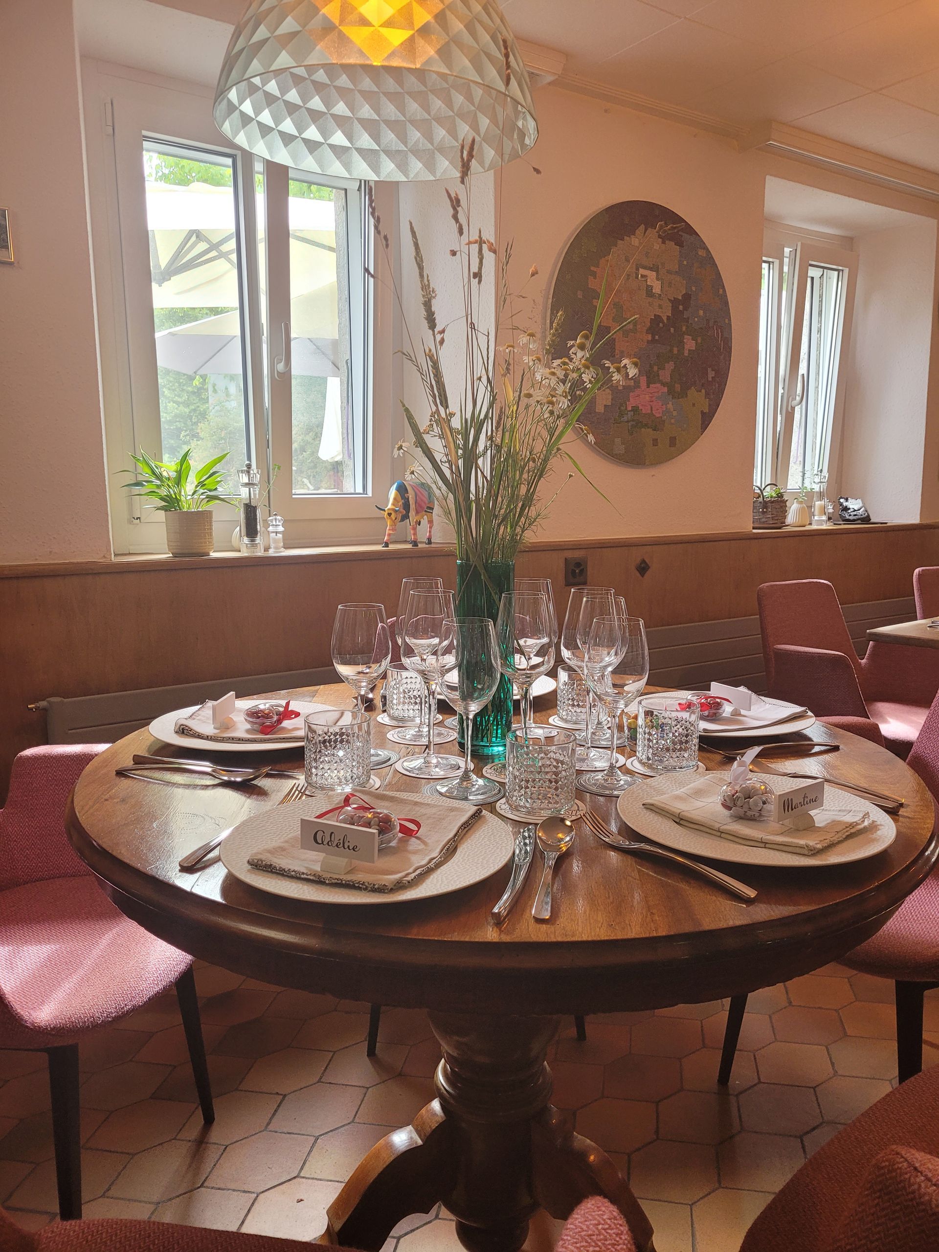 Salle à manger avec table ovale dressée pour le repas, entourée de chaises en velours et transparentes sur un tapis à motifs rouges.