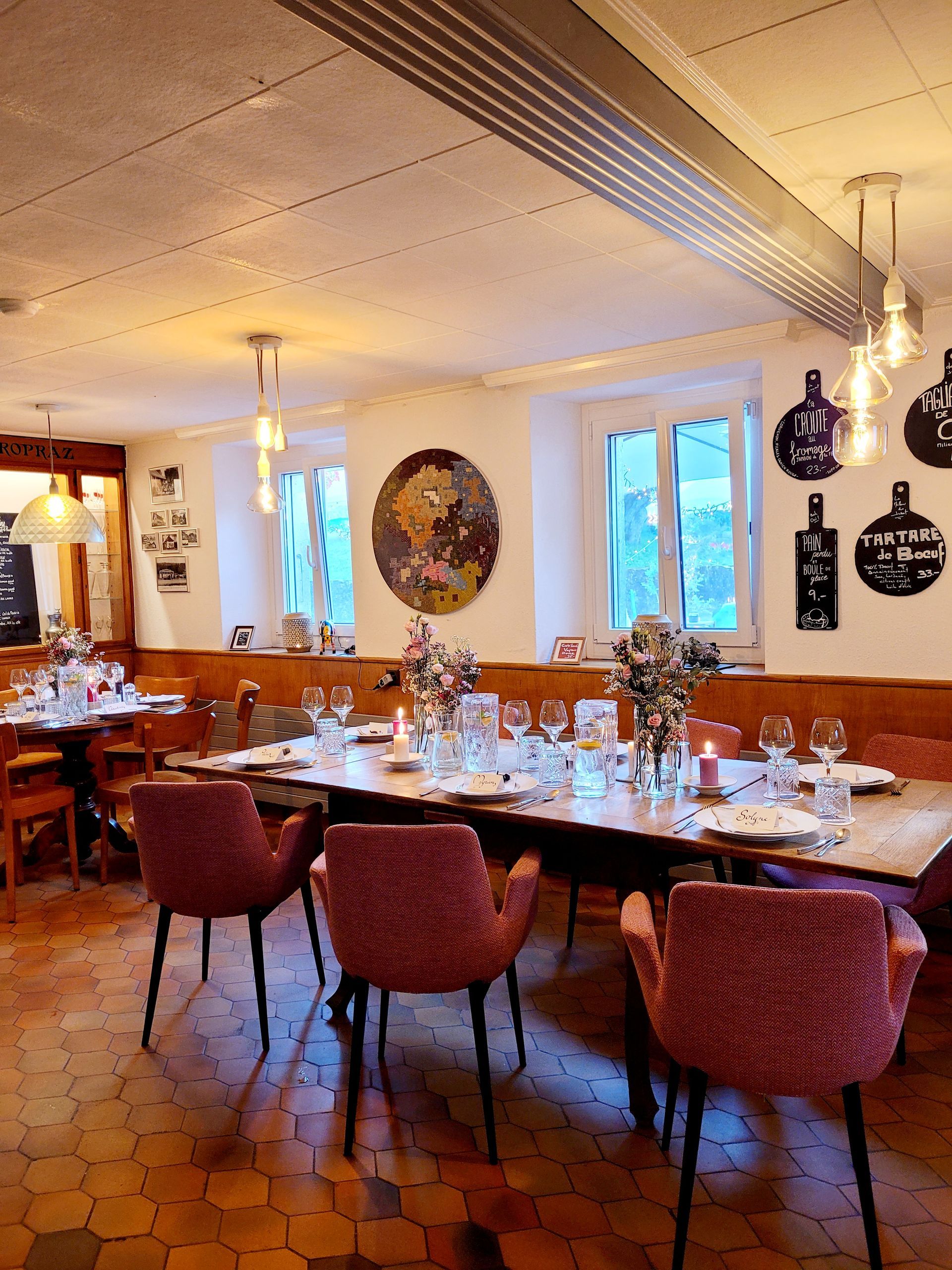 Salle à manger avec une longue table dressée pour un repas, chaises roses, fleurs, bougies et planches à découper décoratives.