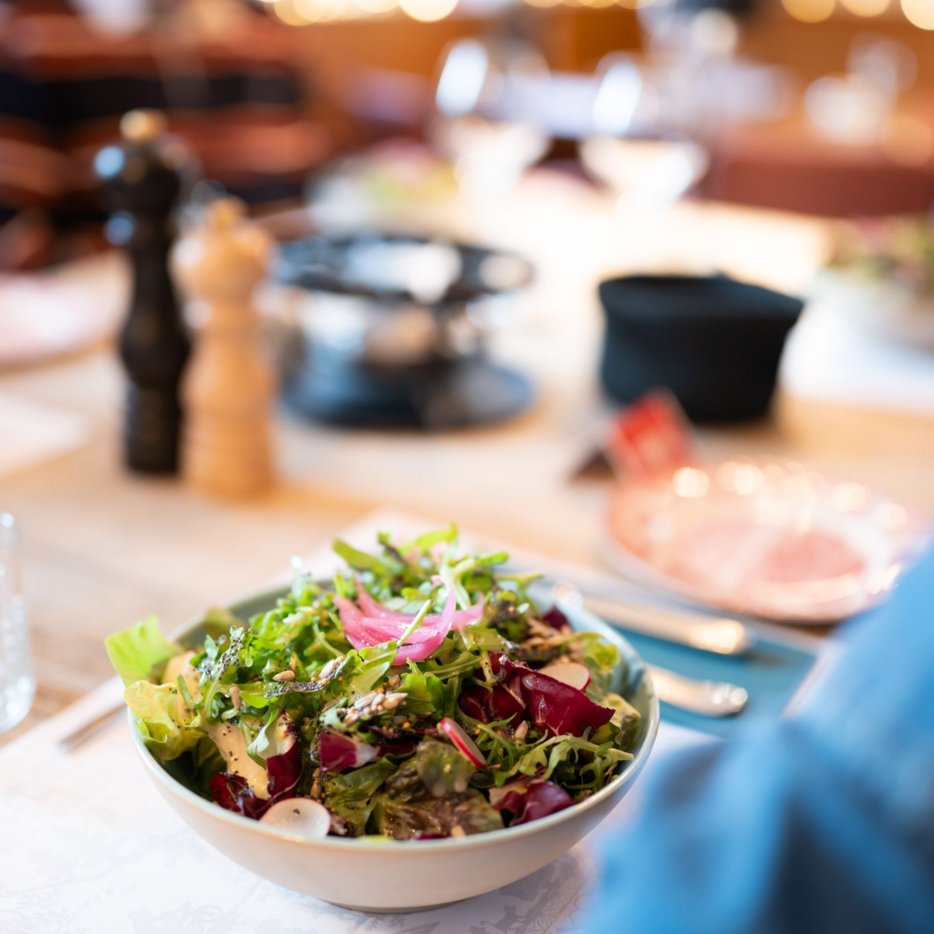 Salade composée d'un mélange de jeunes pousses, de chicorée, de petites graines et de vinaigrette, disposée sur une table.