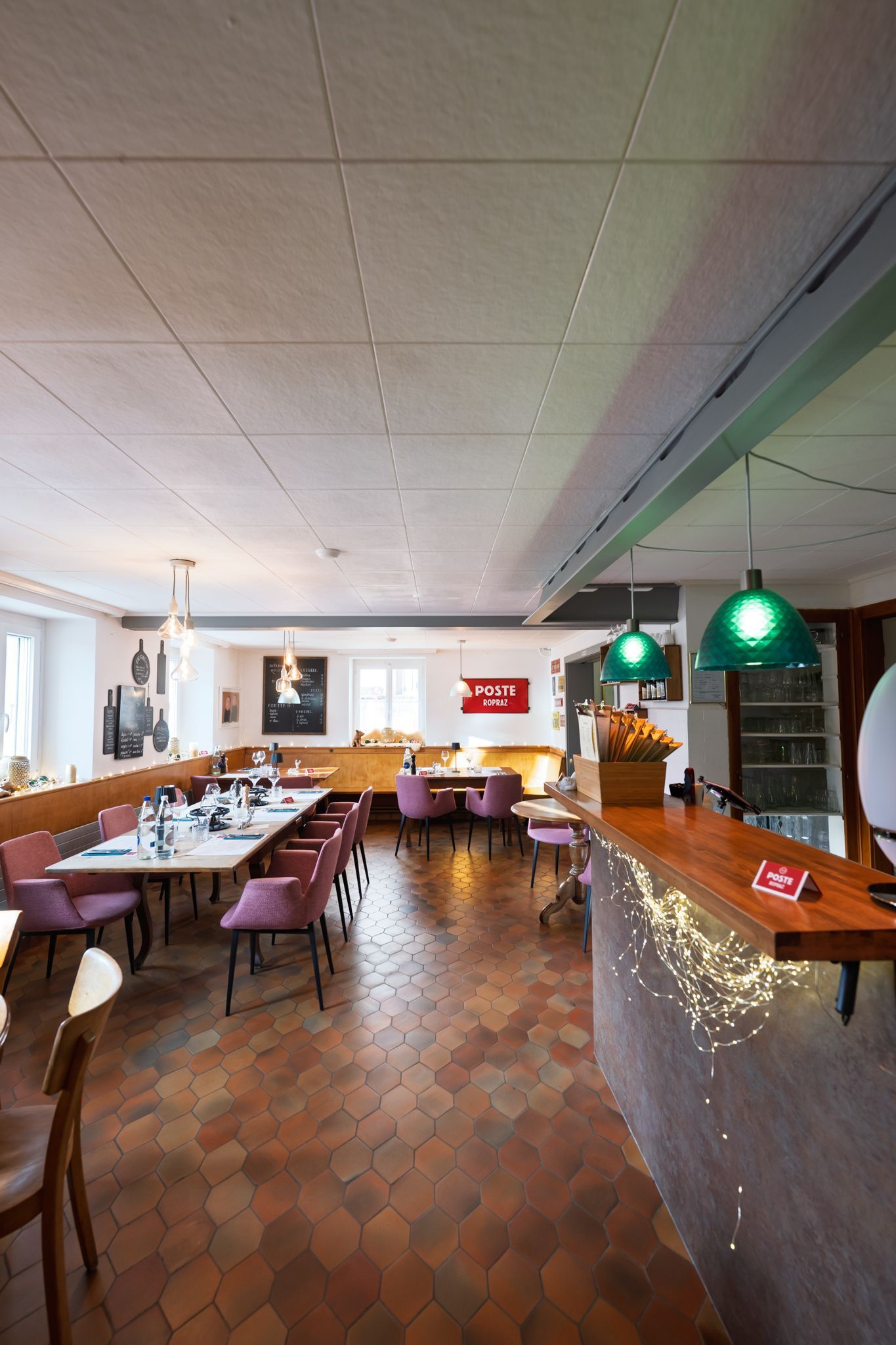 Longue table en bois dressée pour un dîner au restaurant ; guirlandes lumineuses ; planches à découper décoratives au mur.