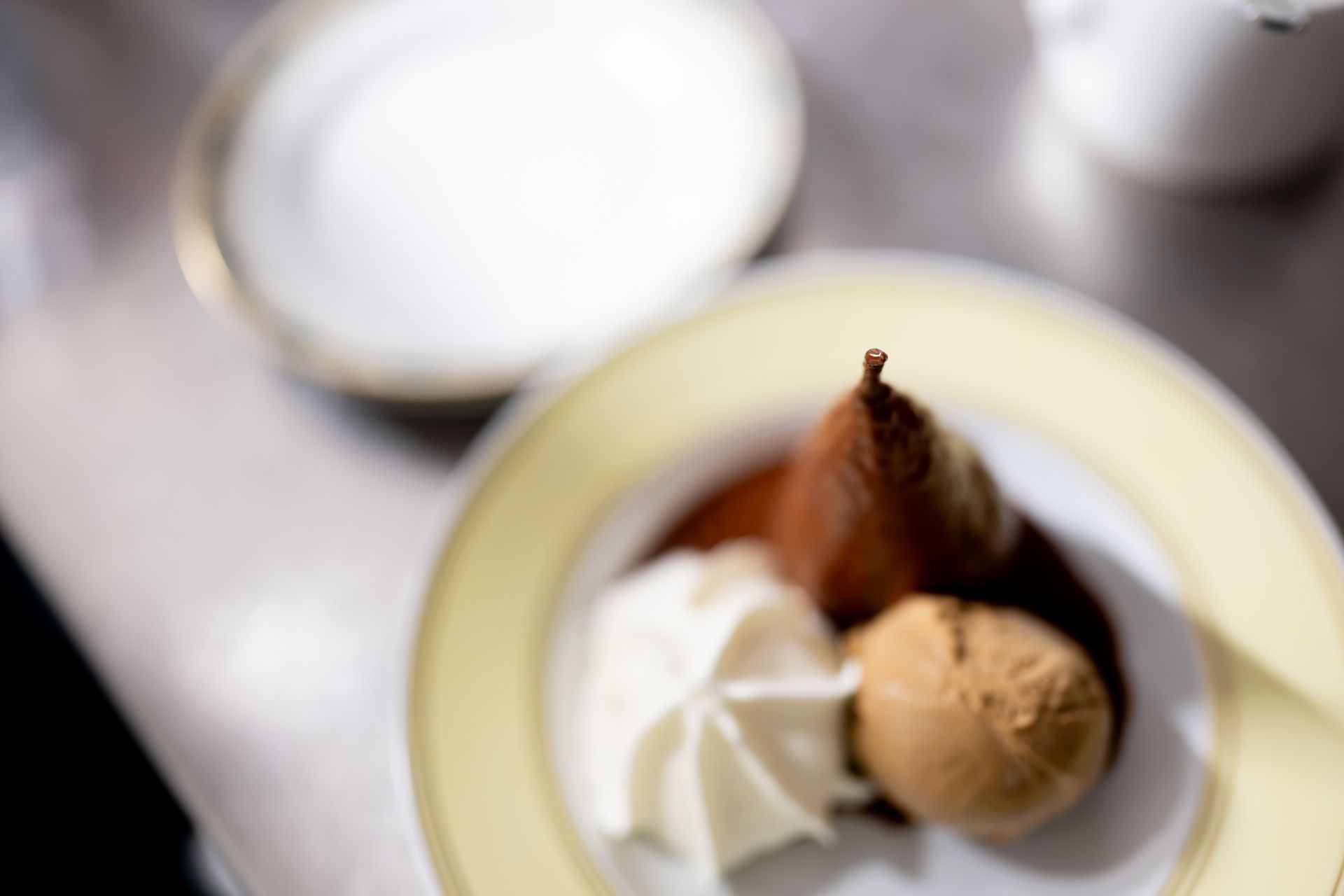 Poire pochée avec boule de glace et quenelle de crème fouettée sur assiette à bord jaune pâle, dessert maison, 
POSTE|ROPRAZ Ropraz