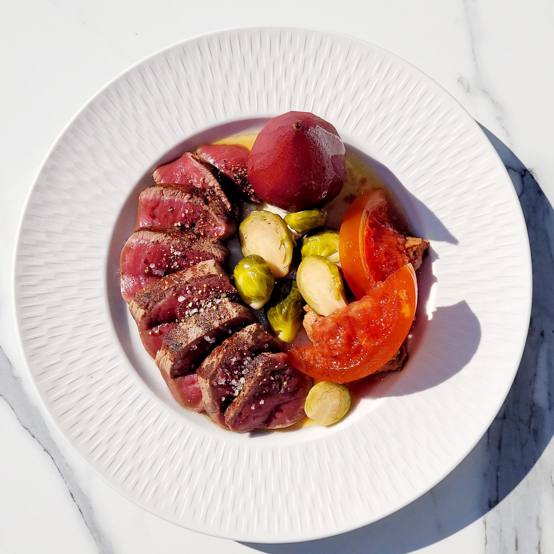 Steak tranché accompagné de légumes, notamment des choux de Bruxelles et des tomates, sur une assiette blanche.