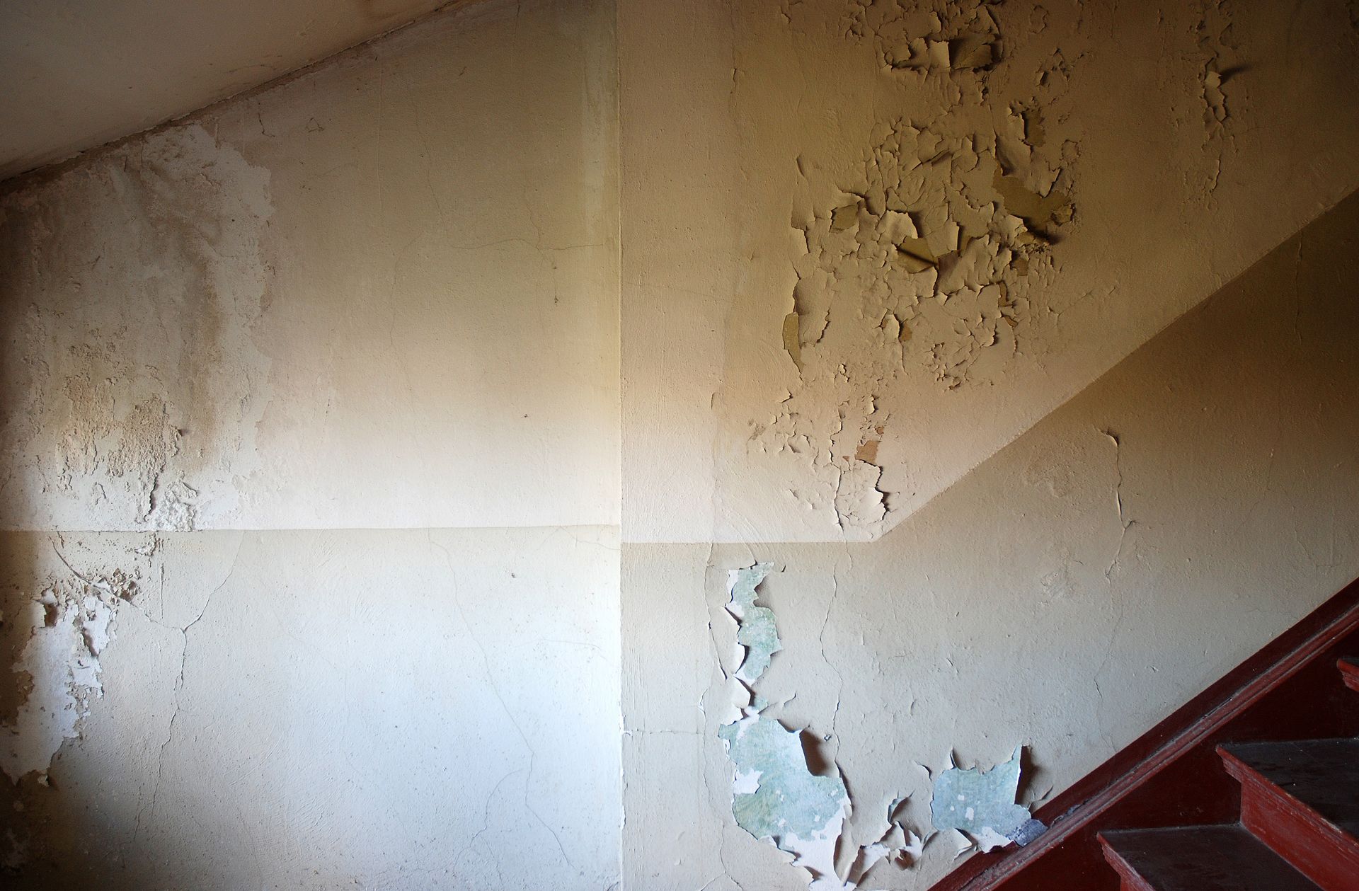 Interior of a building with water damage on the walls, showing peeling paint, discolored patches, and moisture stains.