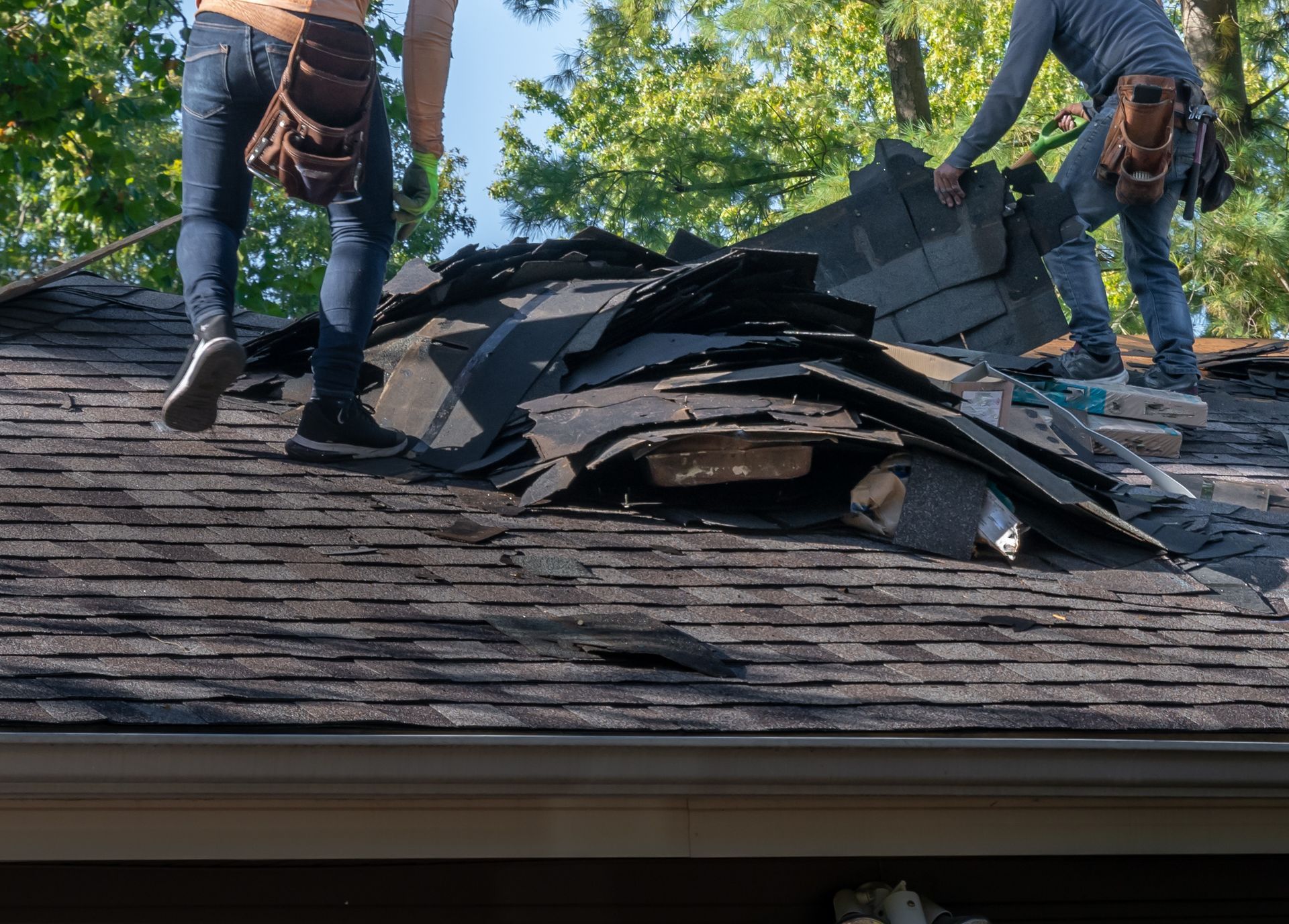 Roofers diligently removing old roofing material from a house, preparing for storm damage repair.