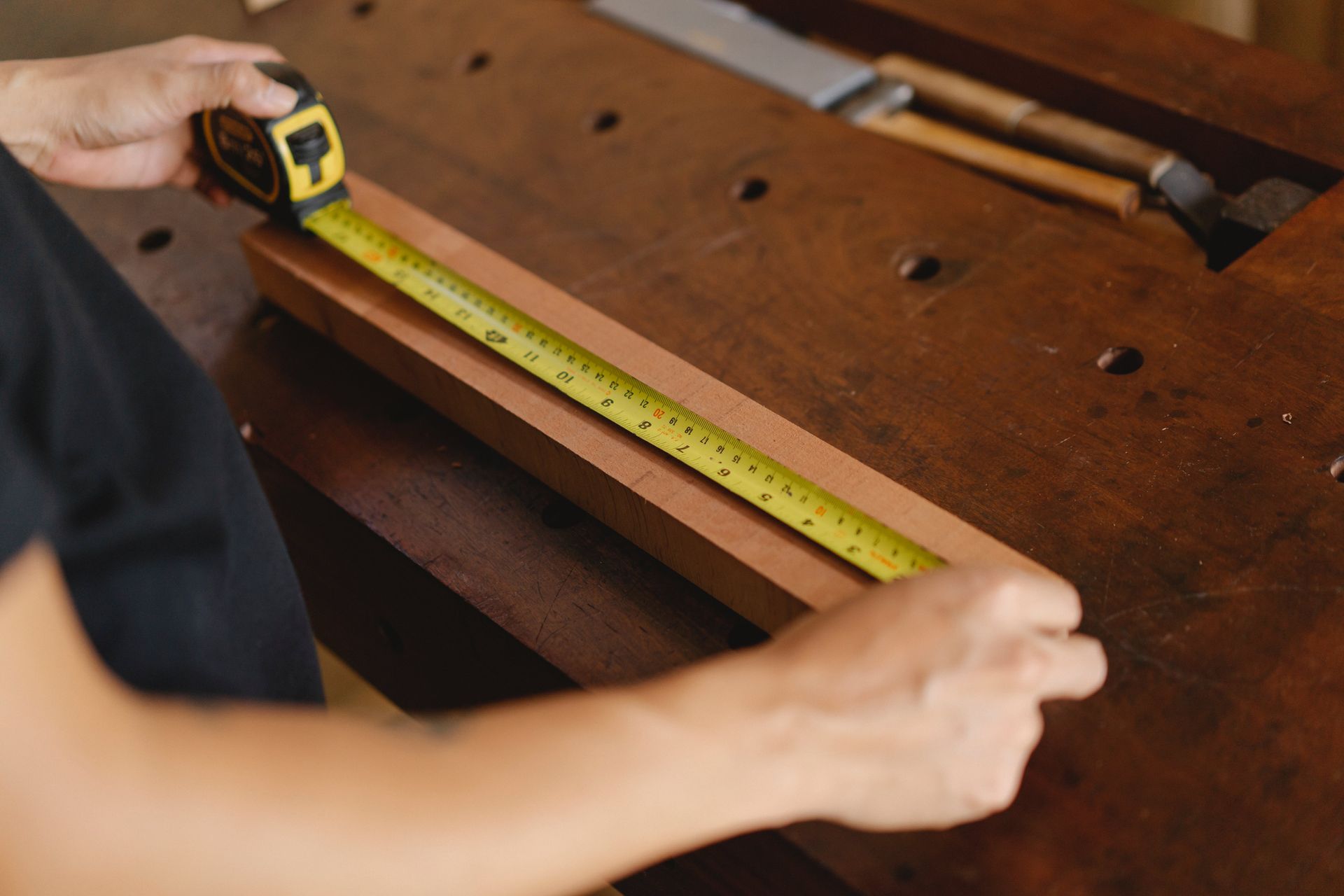 a person measuring a piece of wood with a tape measure