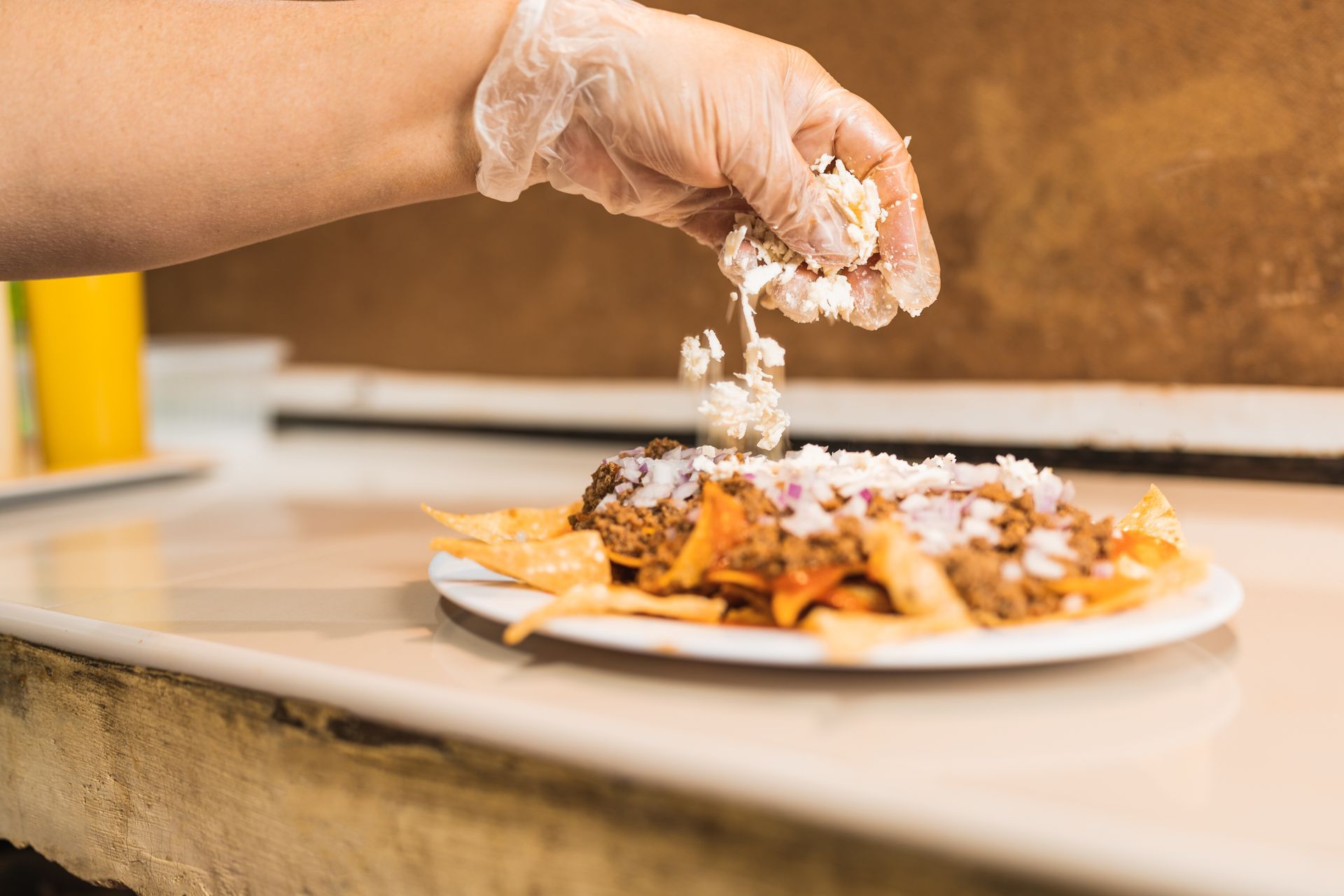 A person is adding cheese to a plate of nachos.