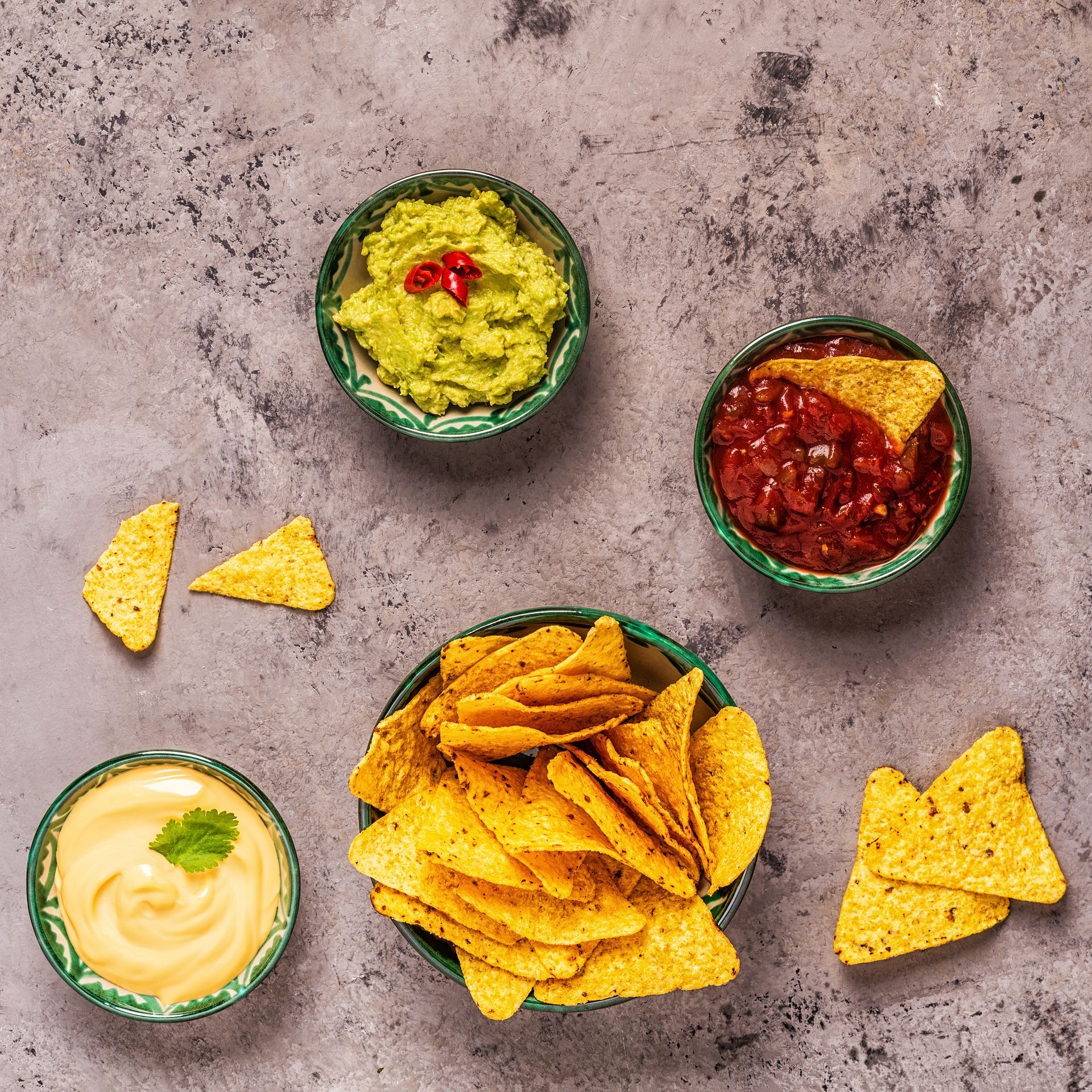 A bowl of nachos with guacamole , salsa , cheese and sour cream.