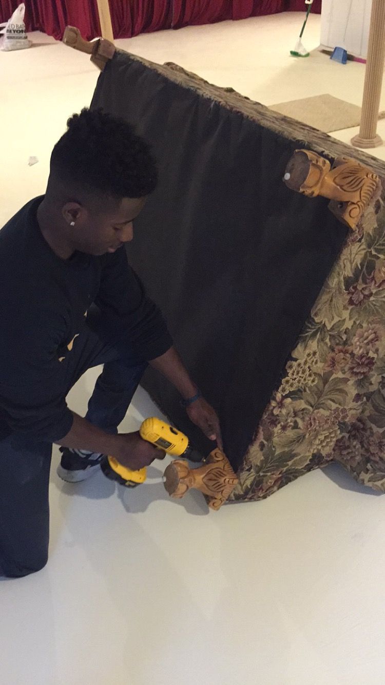 A worker wearing yellow gloves and blue overalls uses a tape gun to seal a cardboard box in a room with moving supplies. A worker wearing yellow gloves and blue overalls uses a tape gun to seal a cardboard box in a room with moving supplies.