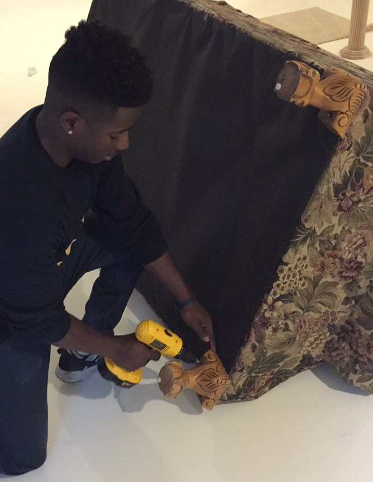 Three workers in blue uniforms move cardboard boxes into the back of a truck.