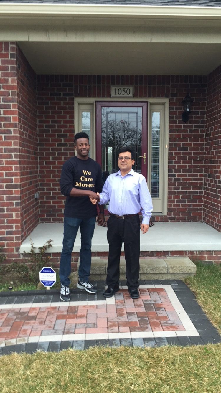 Two movers in blue uniforms loading cardboard boxes into the back of a parked moving truck on a residential street.