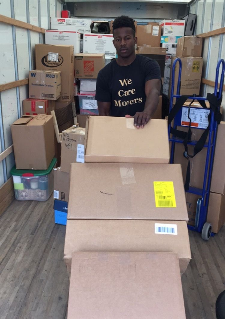 Movers loading cardboard boxes into a truck while a couple stands nearby at a residential home.