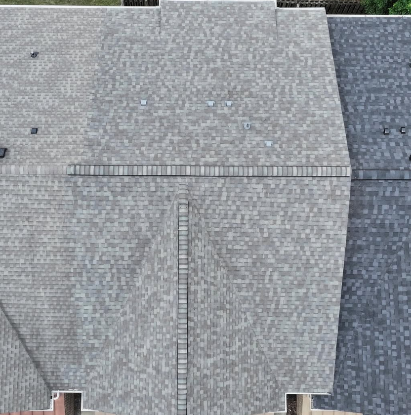 Overhead view of three connected house roofs with gray shingles, a brick chimney, and various vents.