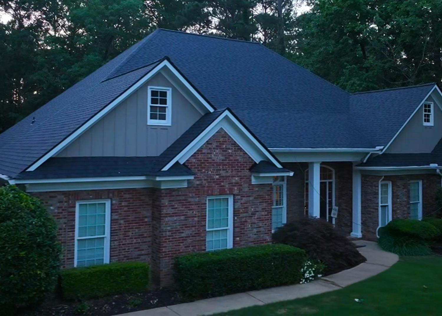 House with brick and tan siding, a dark blue roof, and white trim, in a green, landscaped yard.