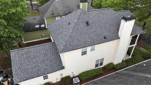 Aerial view of a light beige two-story house with a dark gray shingled roof and a large white chimney.