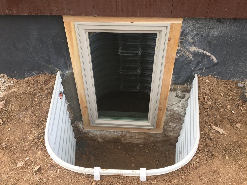 A window is being installed in a basement window well.