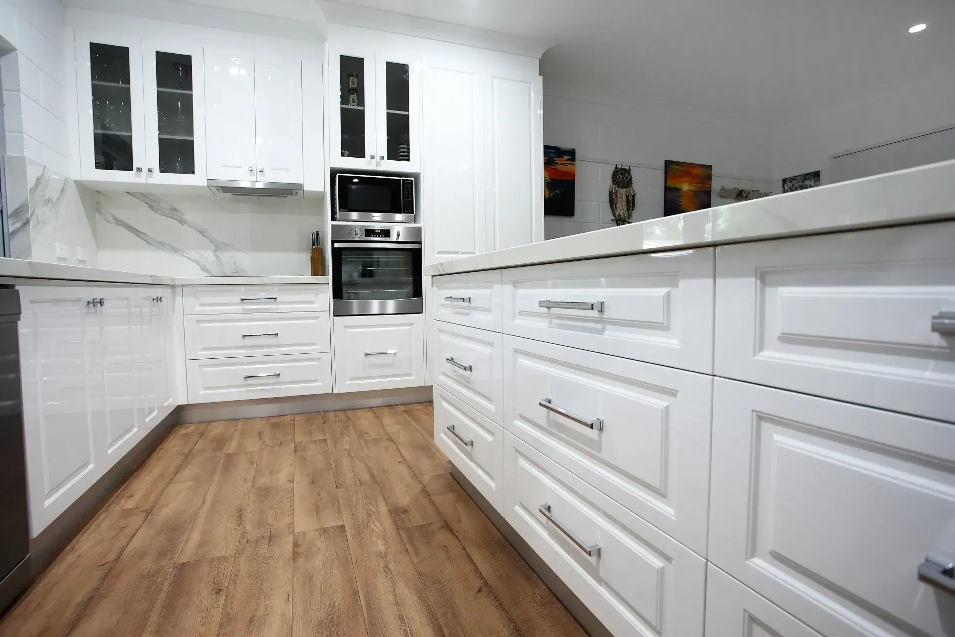 White Kitchen With Wood-look Floors, Cabinets, And Island With Stainless Steel Appliances And Marble Backsplash — B & C Cabinets in Mareeba, QLD