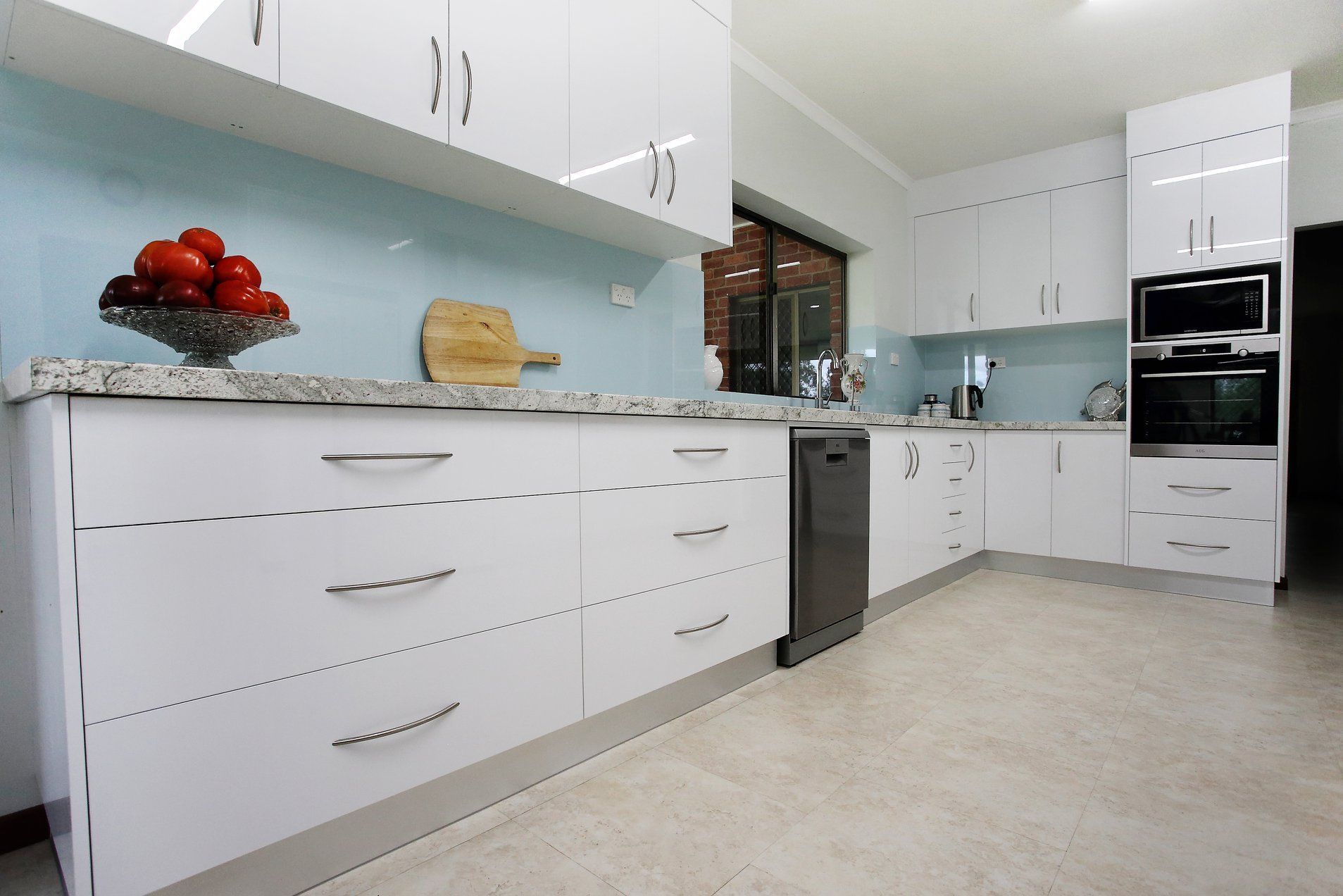 Modern White Kitchen With Granite Countertops, Stainless Steel Appliances, And Blue Glass Backsplash — B & C Cabinets in Mareeba, QLD