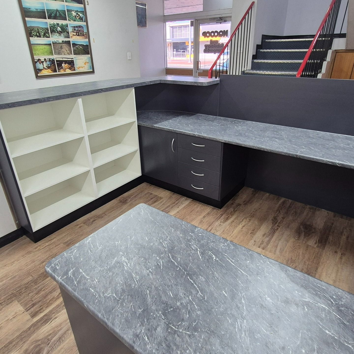 L-shaped Office Desk With Gray Countertop And Cabinets. Shelves On The Left. Staircase In The Background — B & C Cabinets in Mareeba, QLD