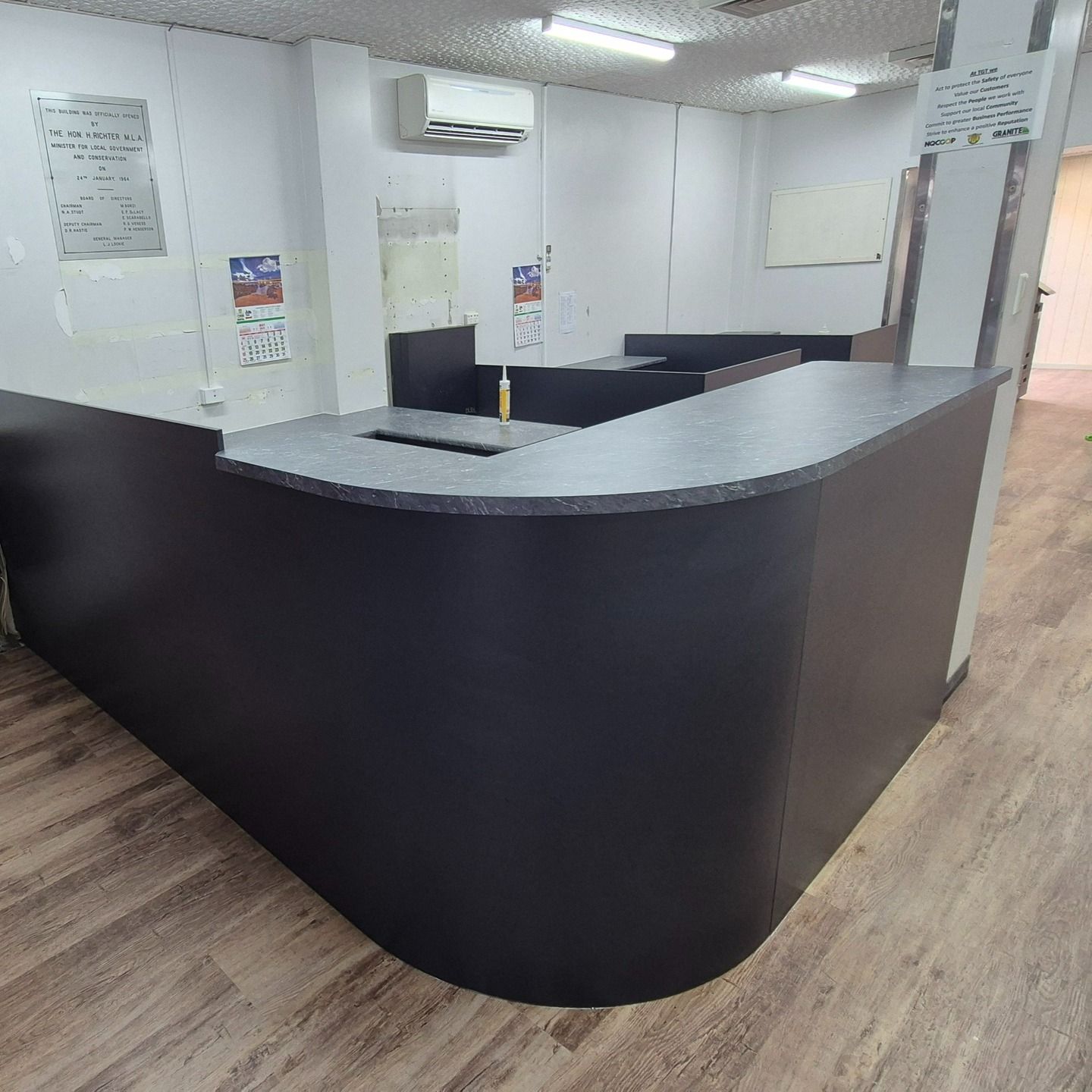 Black Reception Desk In A Room With Light Wood Flooring. White Walls, Overhead Lighting — B & C Cabinets in Mareeba, QLD
