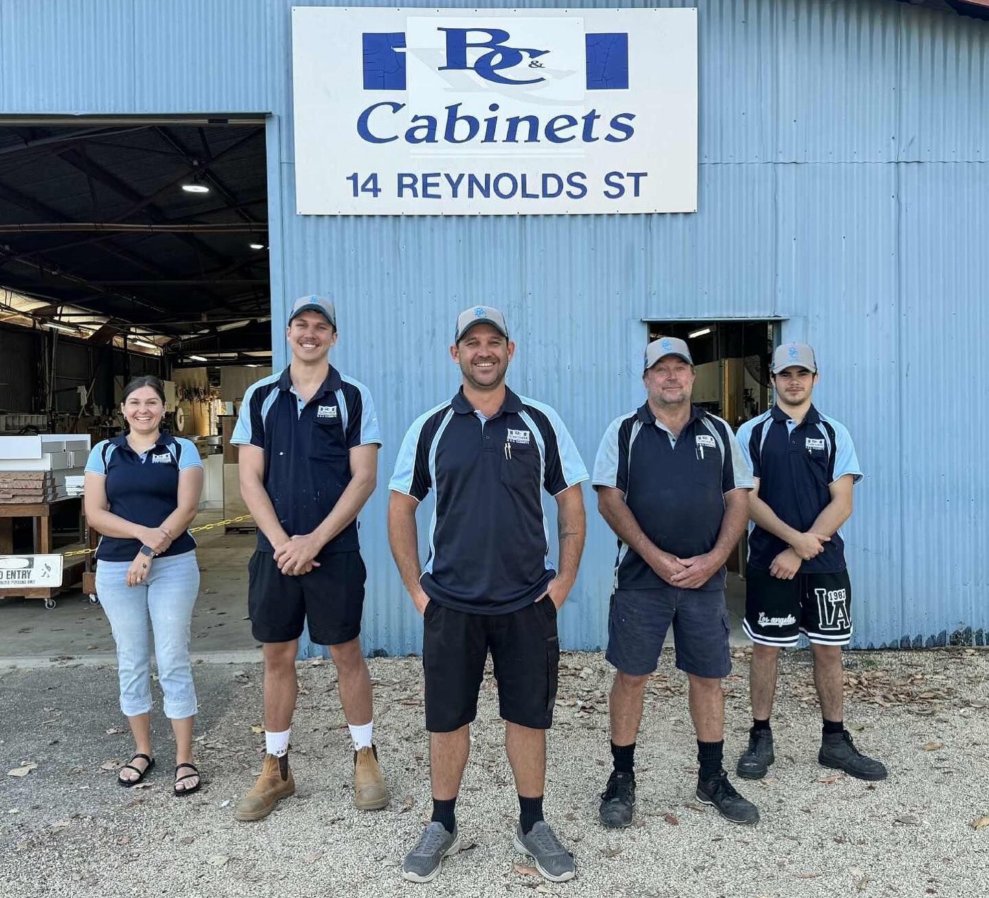 Five people in company uniforms stand in front of a blue industrial building labeled 