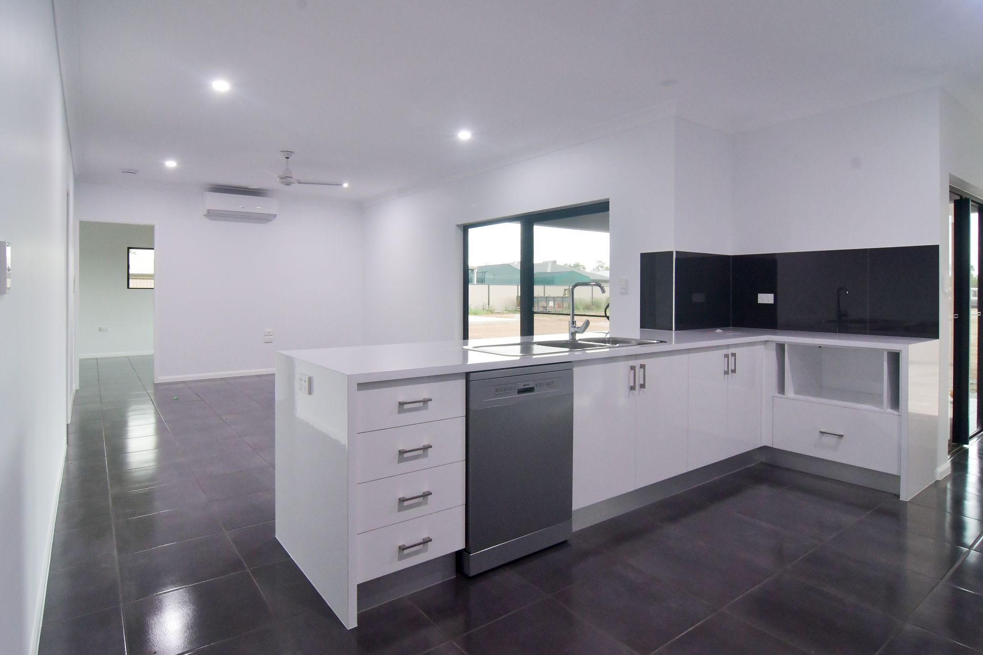 A Bright, Modern Kitchen With White Cabinetry, Stainless Steel Dishwasher, Black Splashback, And Glossy Dark Tile Floors — B & C Cabinets in Mareeba, QLD