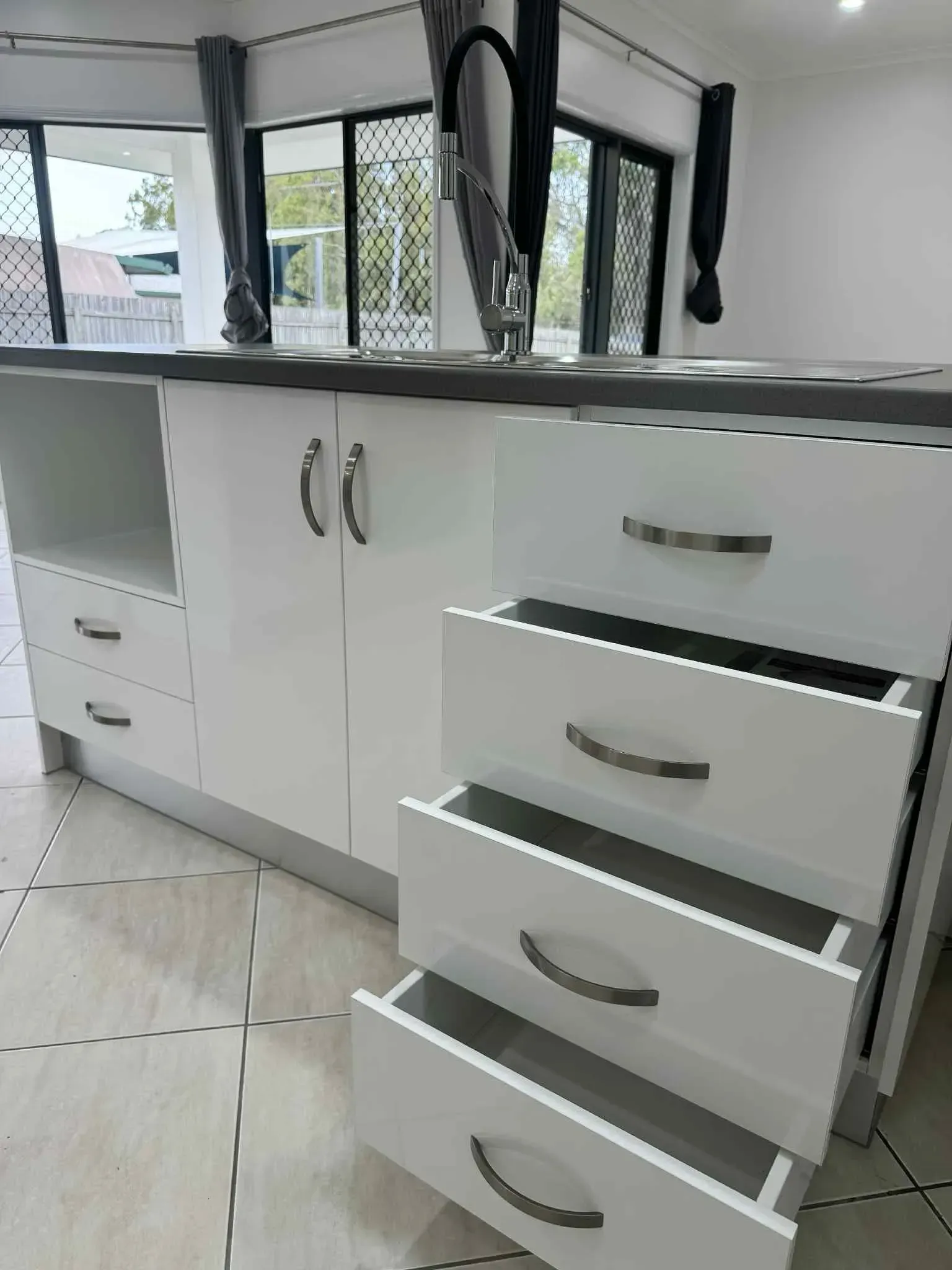 White Kitchen Cabinets With Drawers And Doors, Gray Countertop, And A Black Faucet — B & C Cabinets in Mareeba, QLD