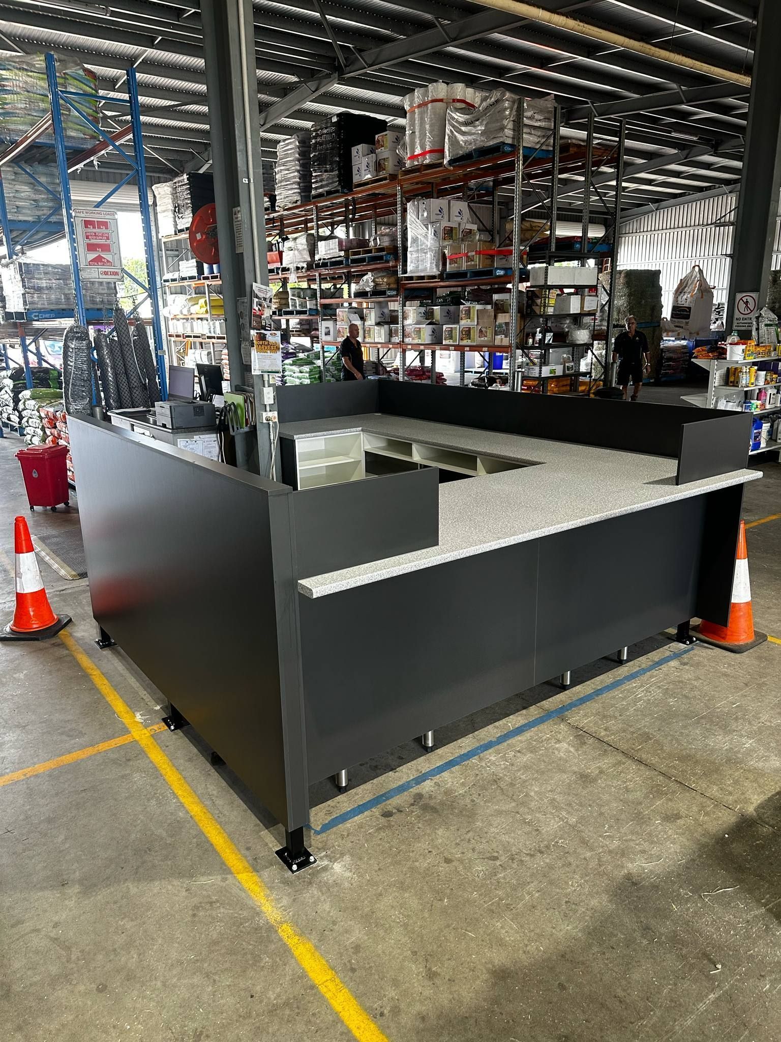 Dark Gray Retail Display Counter In A Warehouse, Topped With A Speckled Surface. Orange Traffic Cones Stand Near — B & C Cabinets in Mareeba, QLD