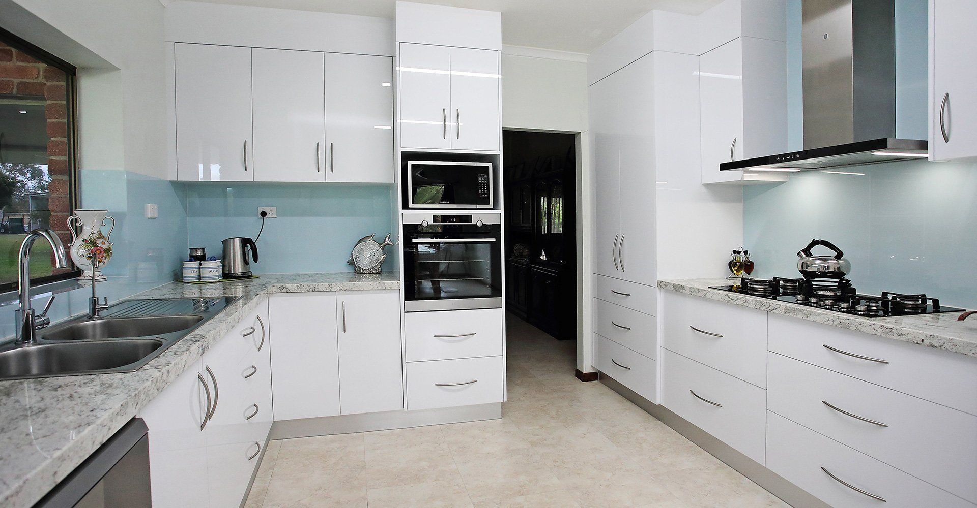 Modern White Kitchen With Stainless Steel Appliances, Light Blue Backsplash, Granite Countertops — B & C Cabinets in Mareeba, QLD