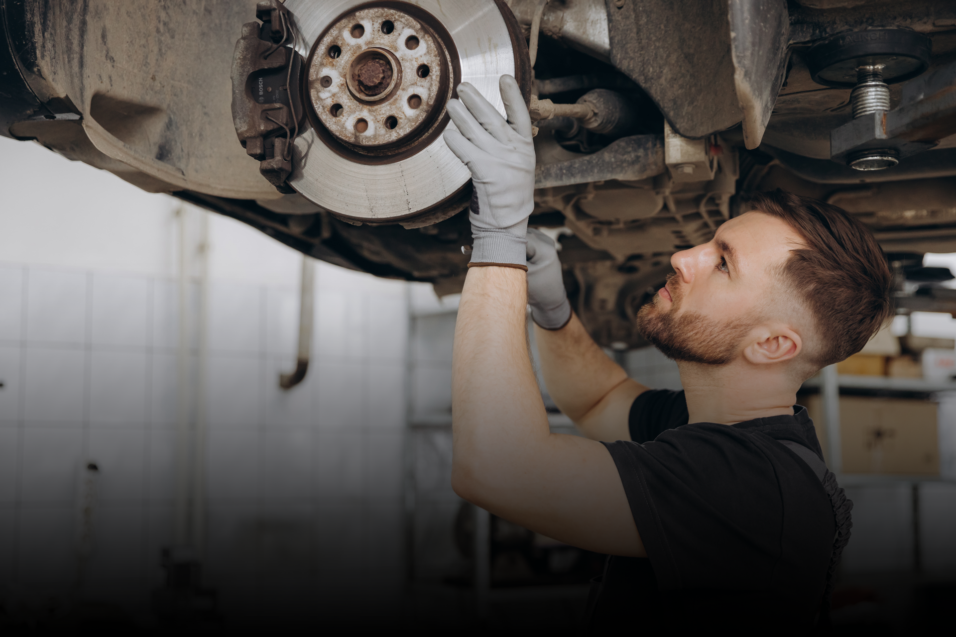 Technician examining vehicle brake system on lifted car in garage