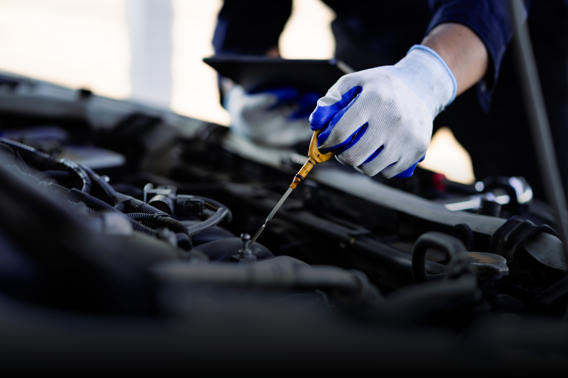 Technician performing oil change using dipstick in engine compartment