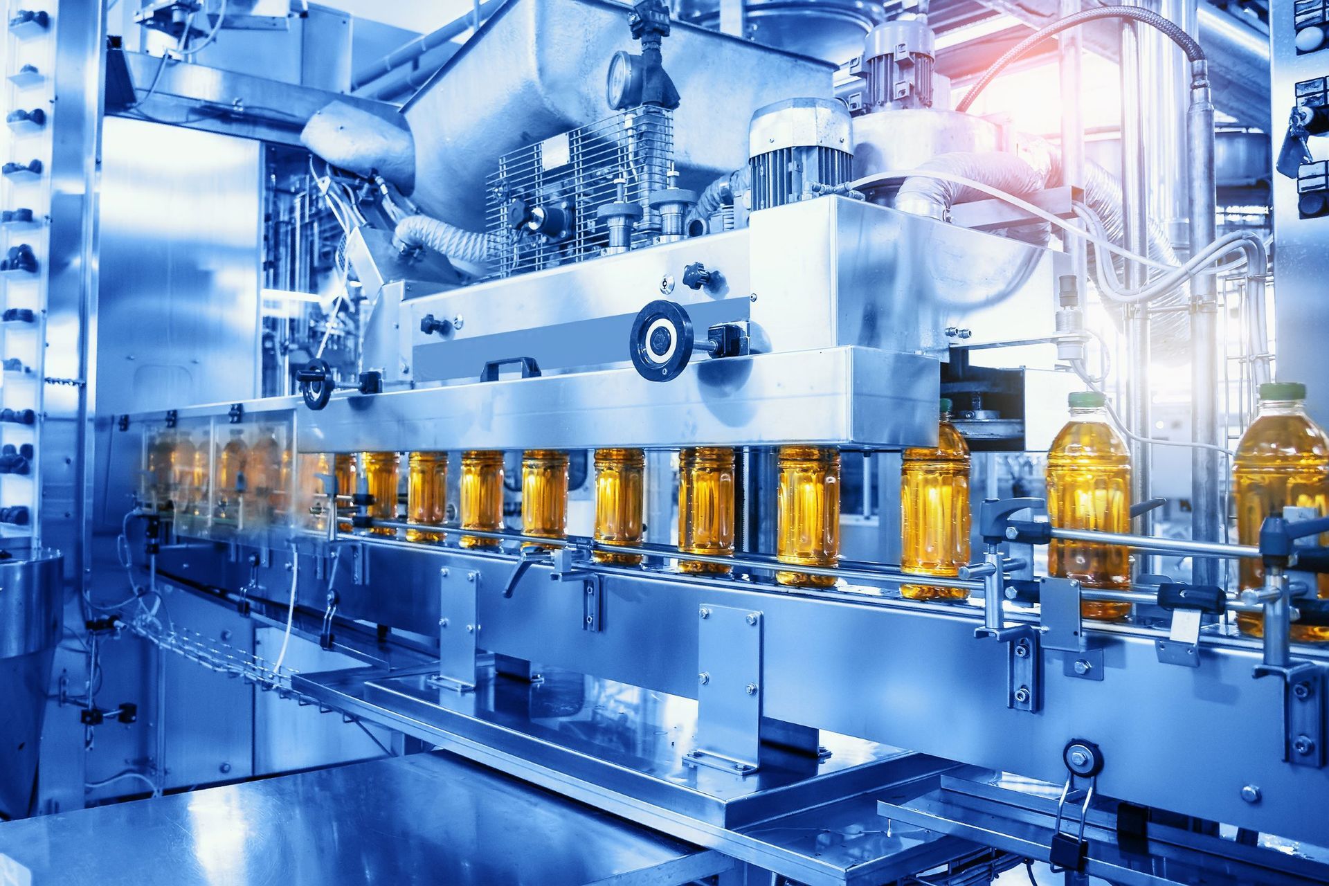 Bottles of golden cooking oil move along an industrial metal conveyor belt in a high-tech manufacturing plant.
