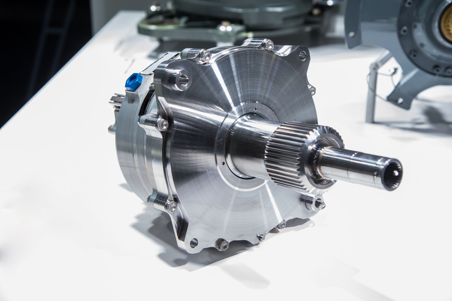 A silver, machined mechanical component with a splined output shaft rests on a white display surface.