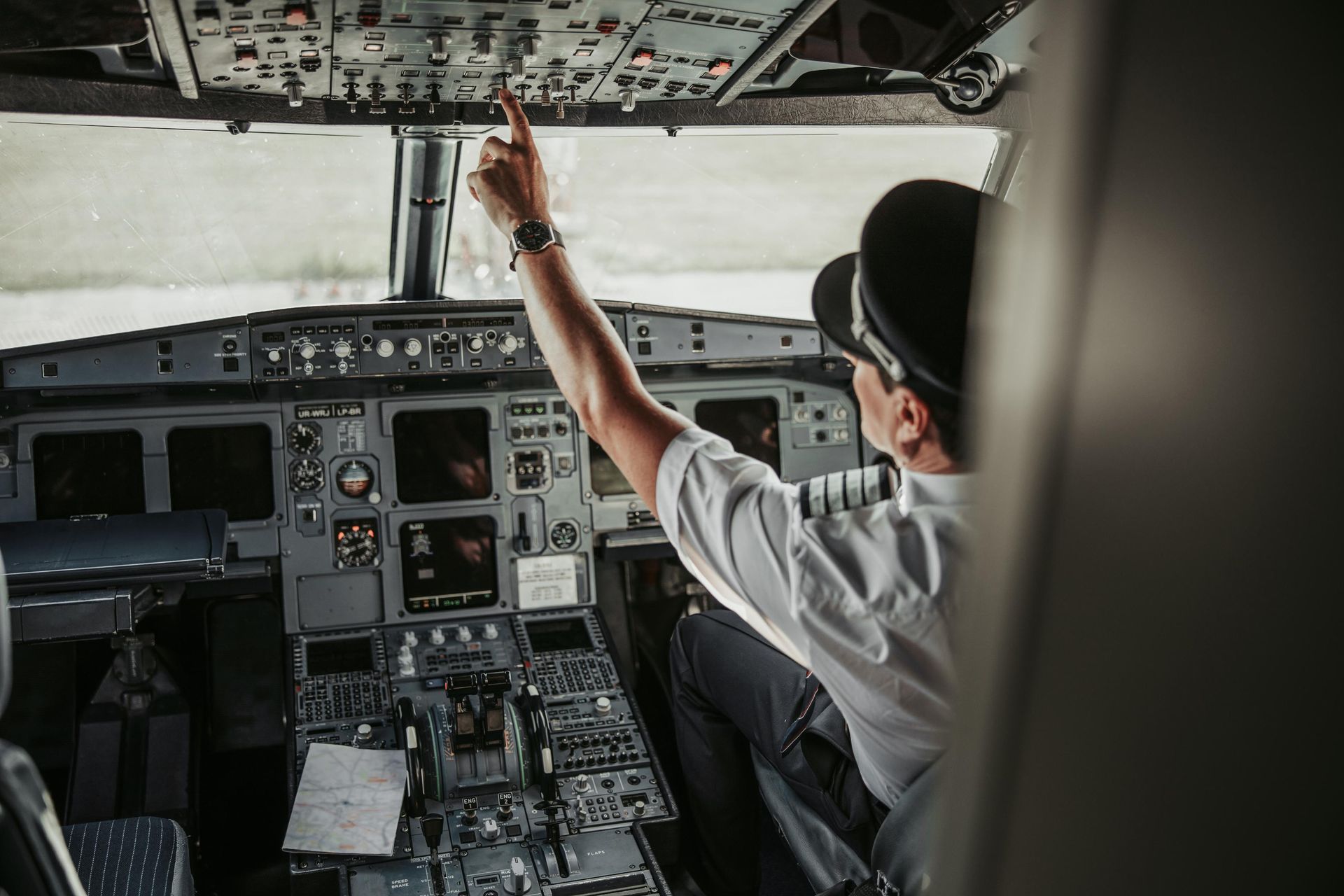 A pilot is sitting in the cockpit of an airplane and pointing at something.