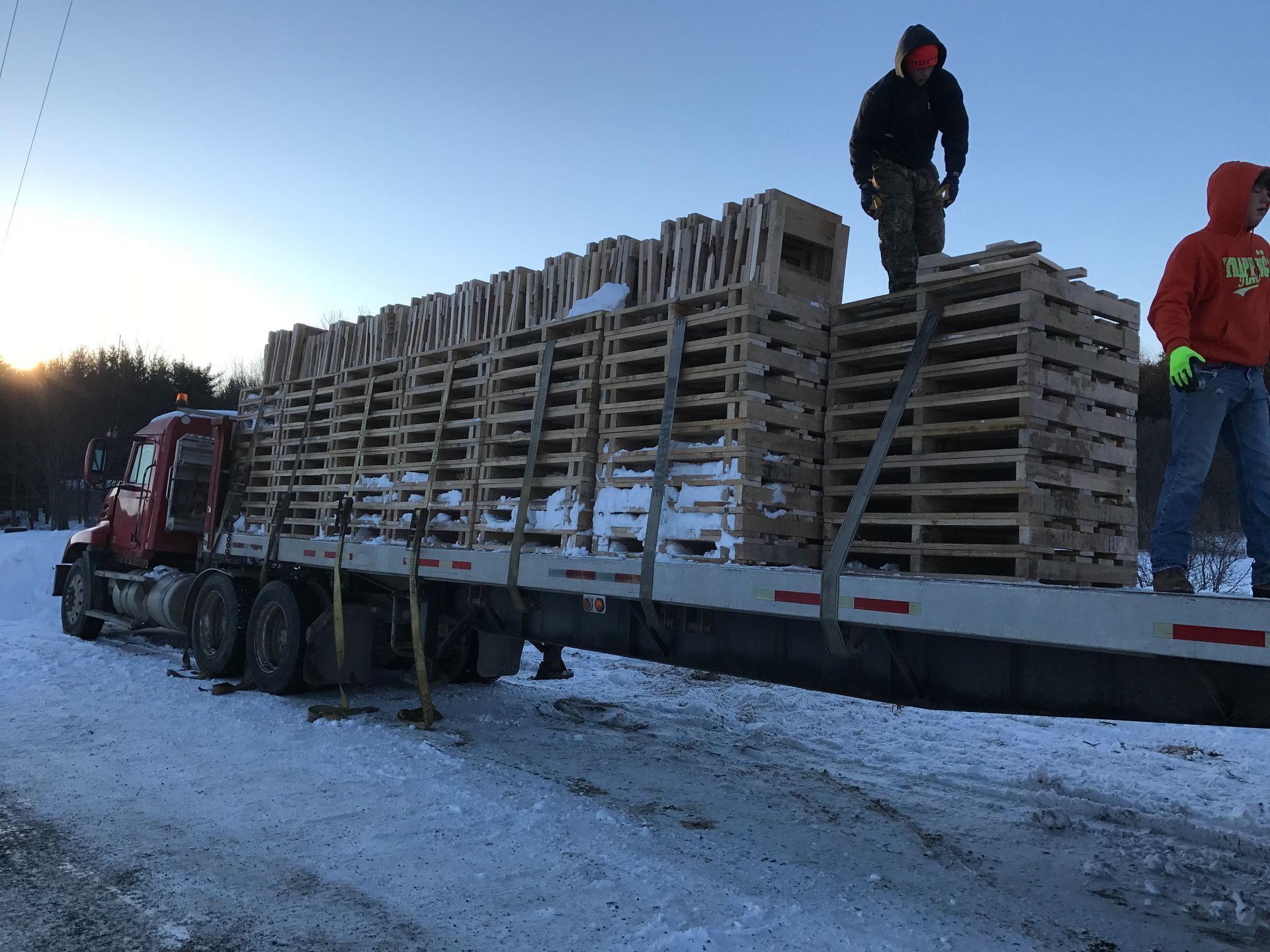 A truck is loaded with wooden pallets on a snowy road.