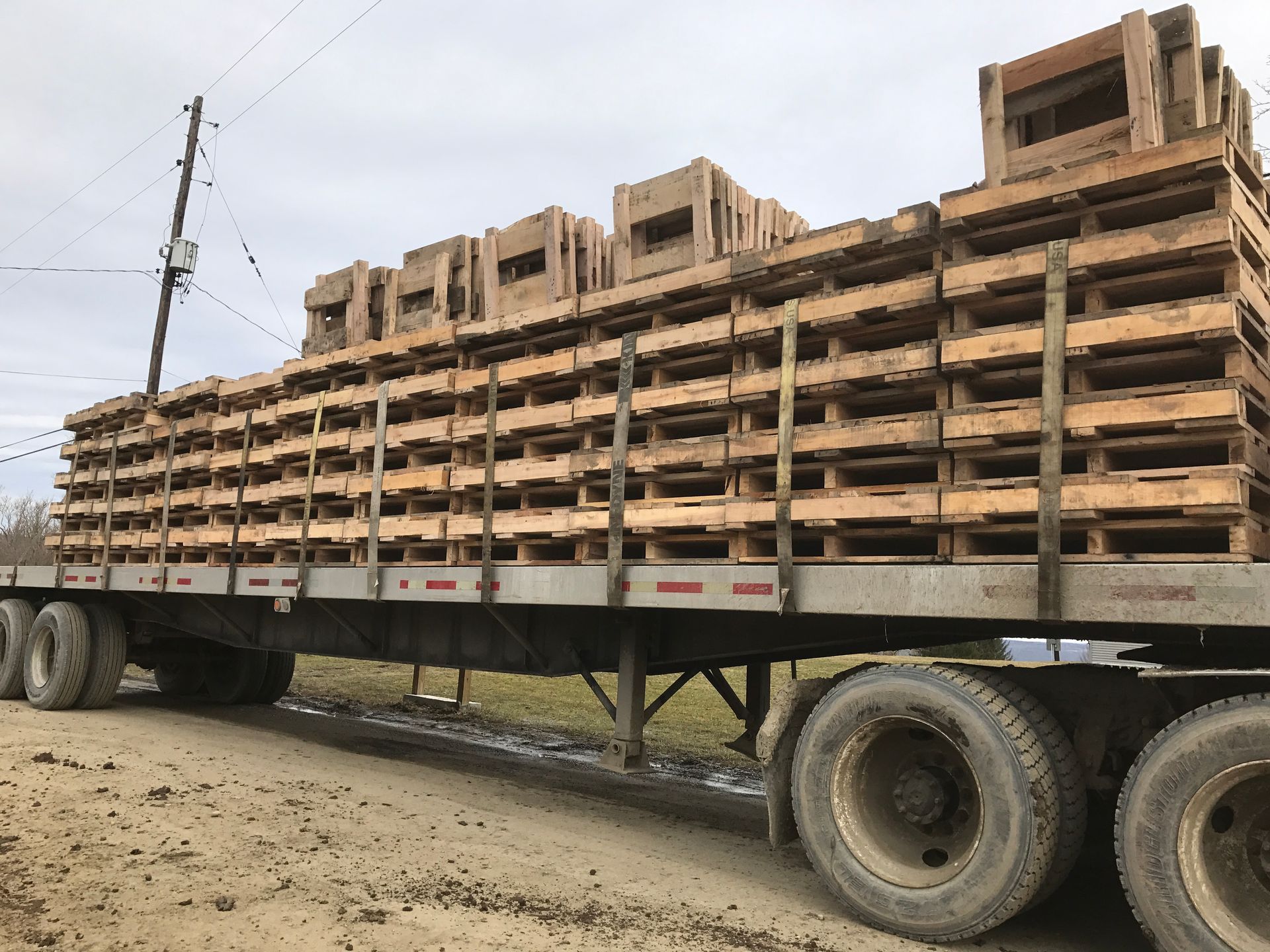A semi truck is loaded with wooden pallets on a dirt road.