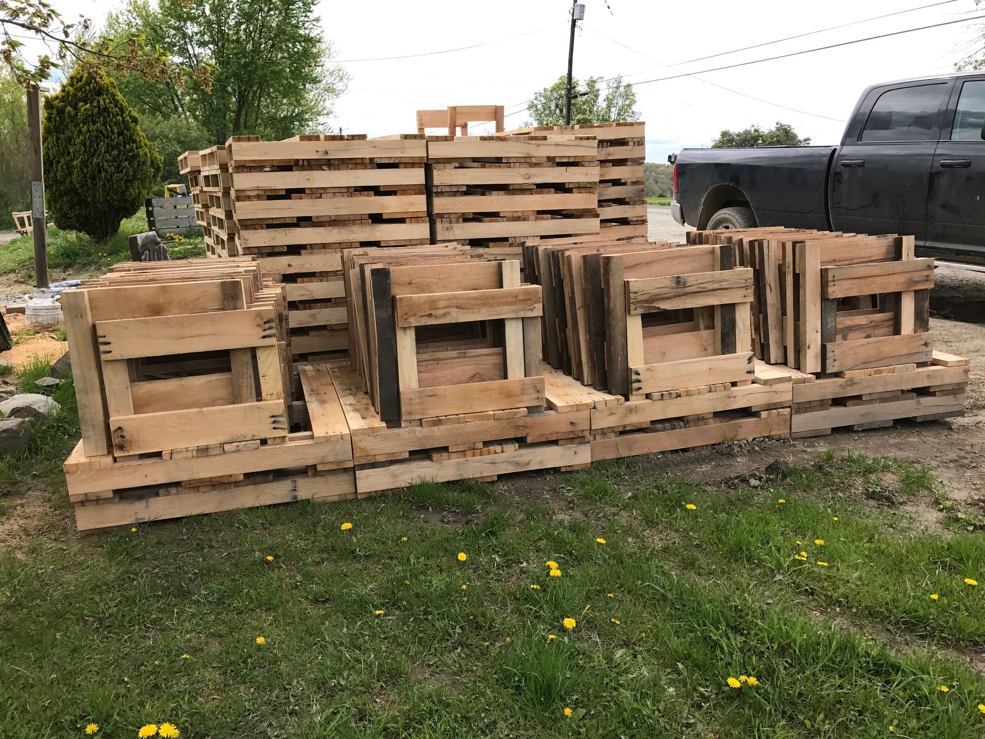 A pile of wooden pallets is sitting in the grass next to a truck.