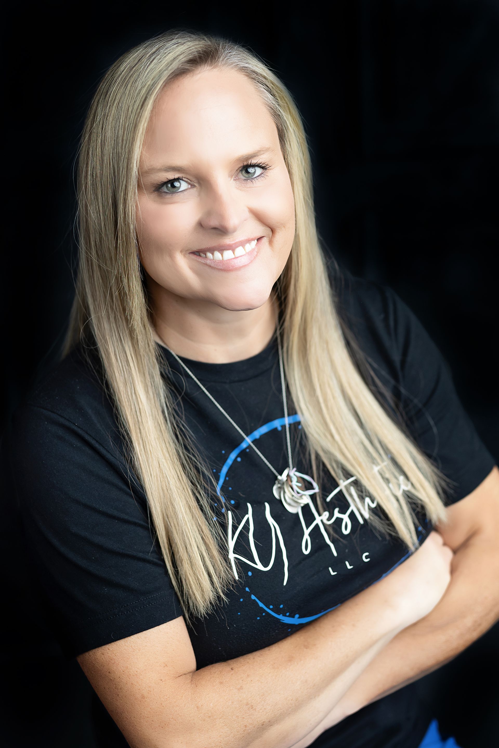 A woman is wearing a black t-shirt and smiling with her arms crossed.