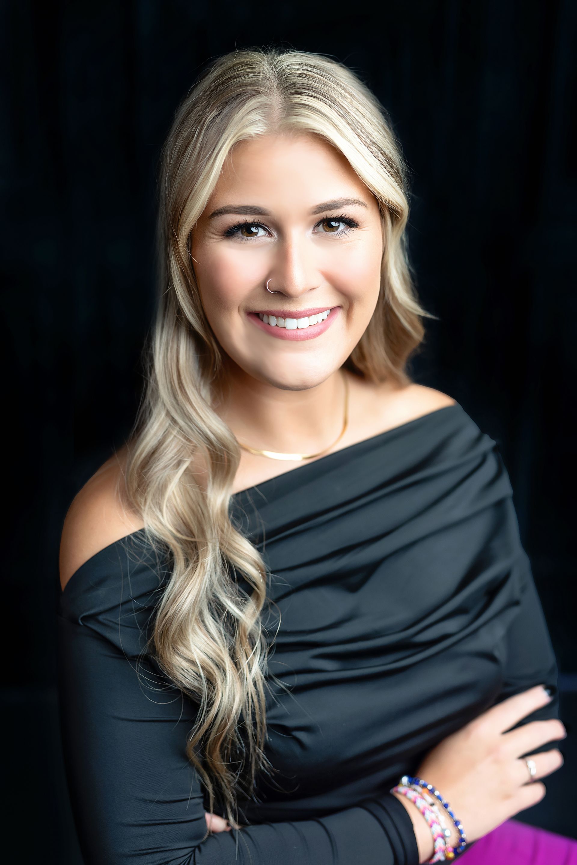 A woman in a black off the shoulder top is smiling for the camera.