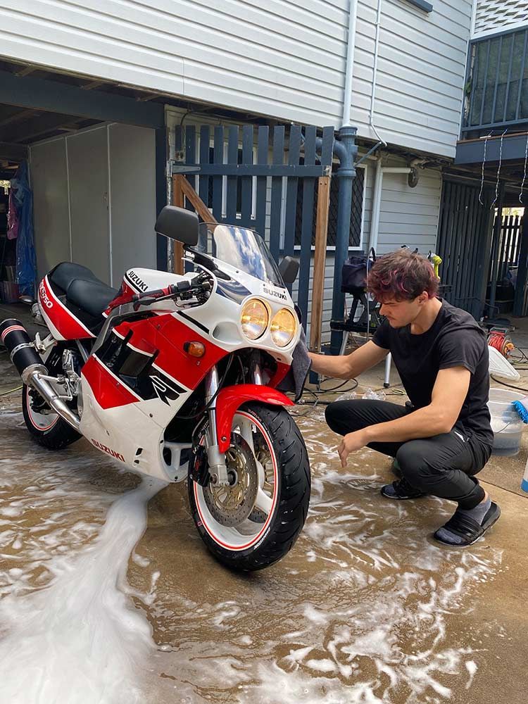 A Man is Kneeling Down to Wash a Red and White Motorcycle — Best Car Detailing in Vincent, QLD