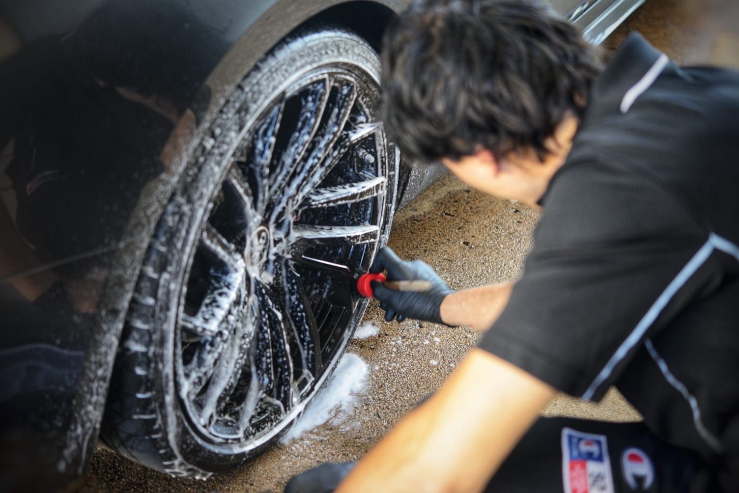 A Person is cleaning the rims of a black car with a brush— Best Car Detailing in Vincent, QLD