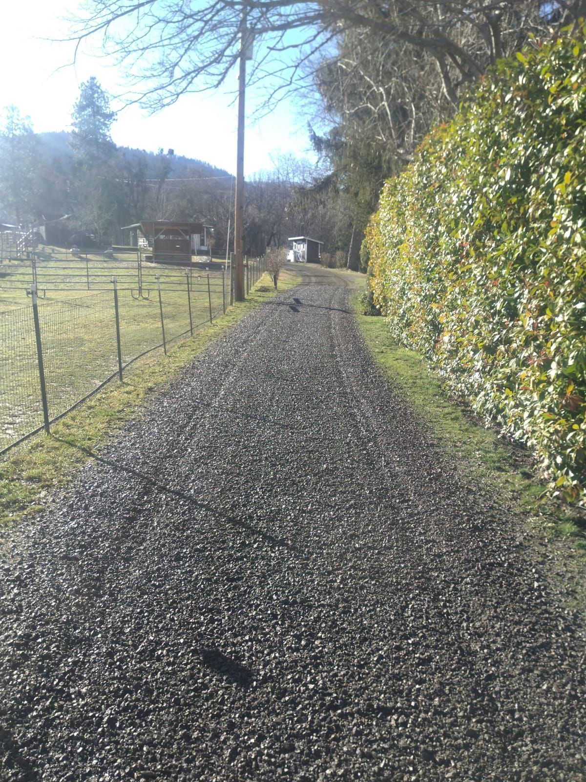 A gravel road going through a field with a fence in the background.